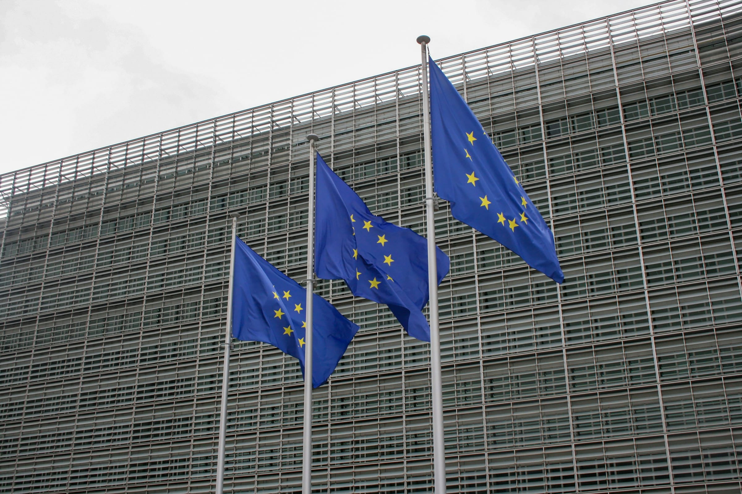 Drei EU-Flaggen wehen vor einem modernen Gebäude in Brüssel, Sitz der Europäischen Kommission